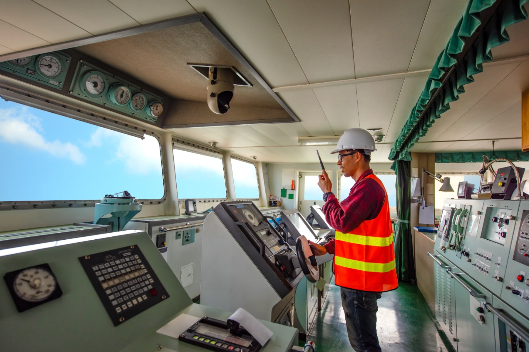 Operador con equipo de protección y radio comunicador navegando una embarcación de transporte energético desde el puente de mando.
